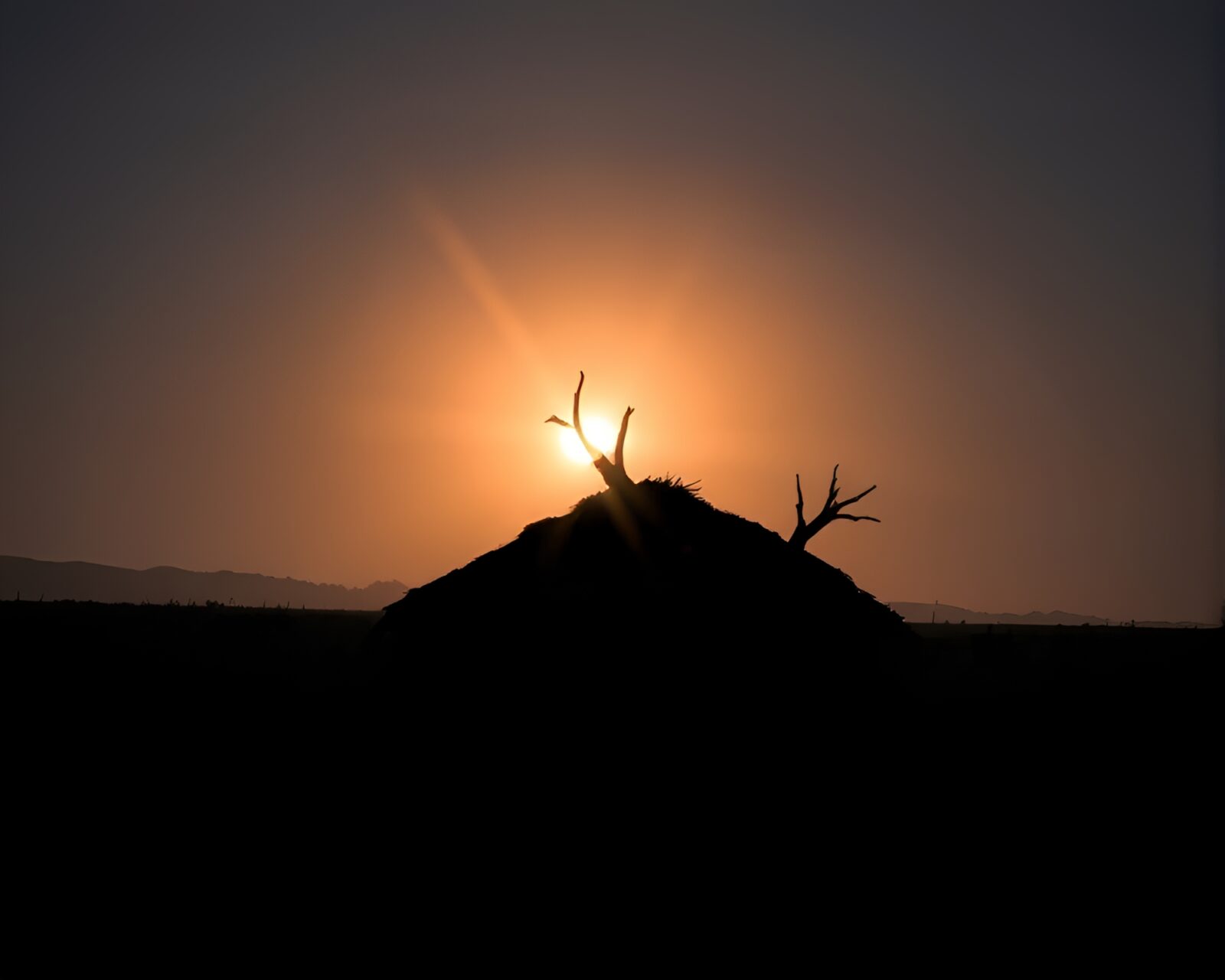 Shadowed mud hut against colorful starburst sky