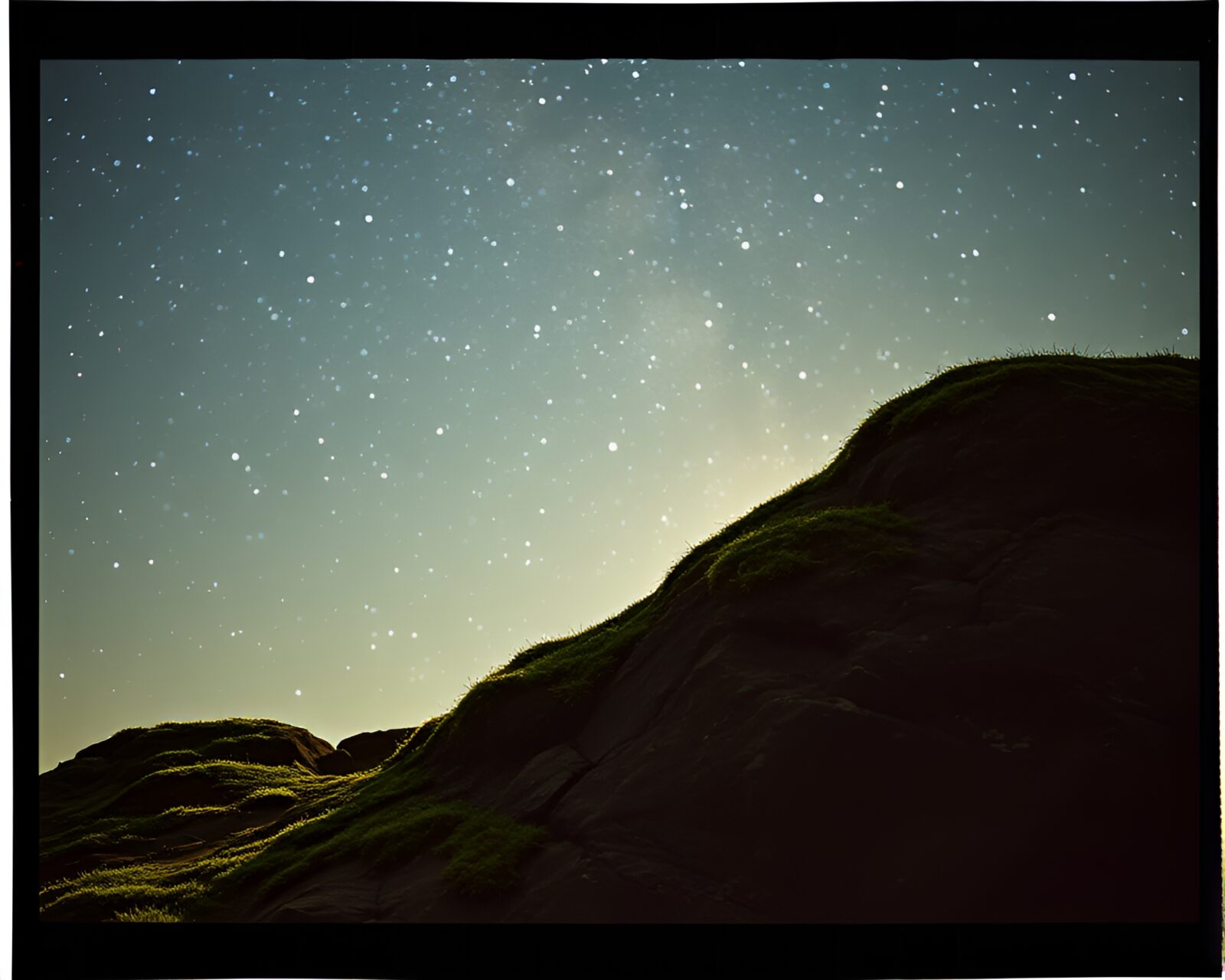 Mossy rock beneath twinkling sky framed by film holes