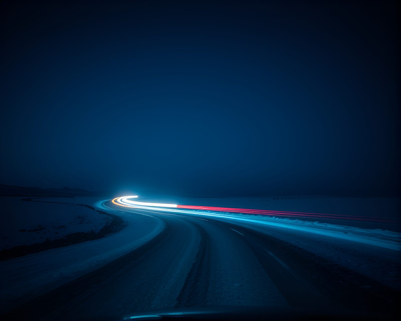 Vibrant car light trails on snowy tundra under sapphire sky